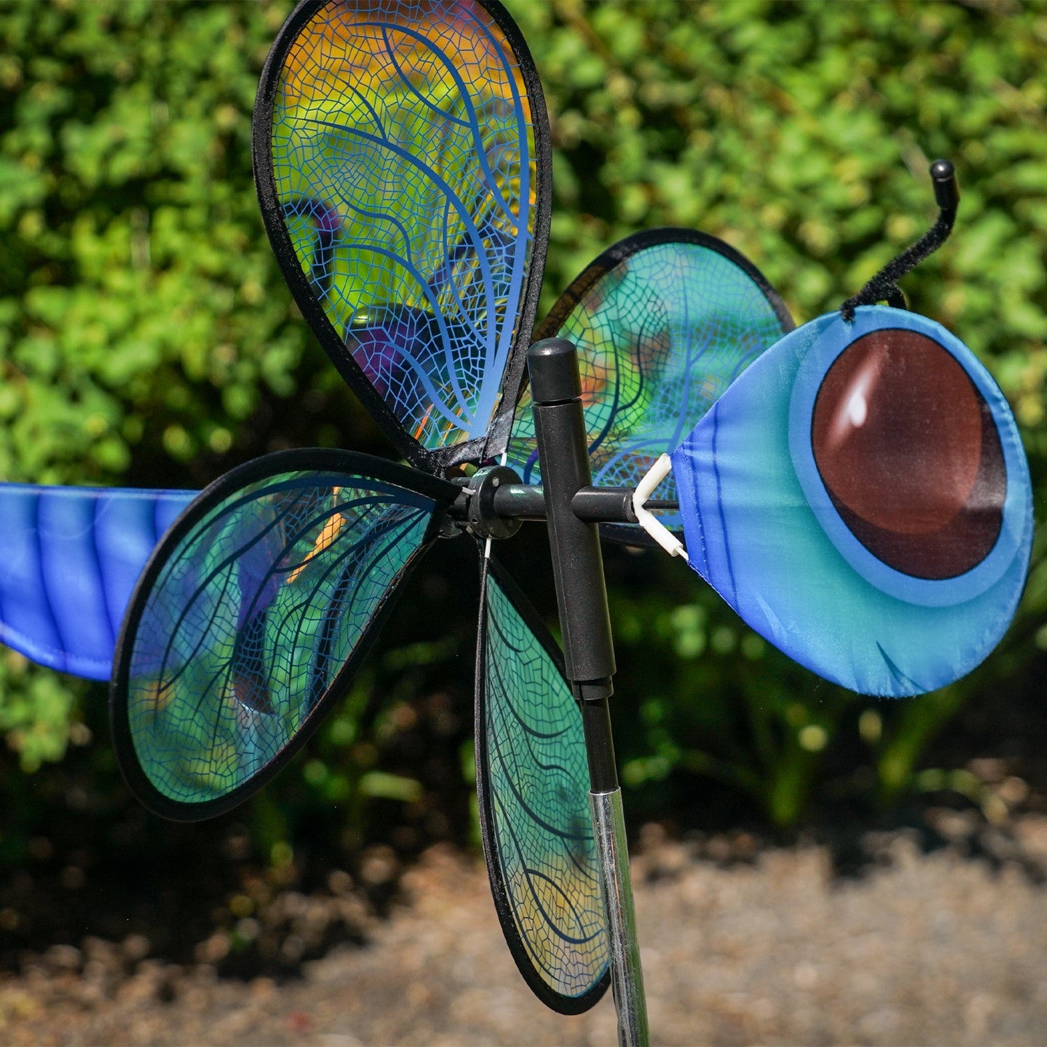 Pivoting Dragonfly Bug Spinner featuring iridescent Mylar wings and a fiberglass frame, elegantly displayed in a vibrant garden setting.