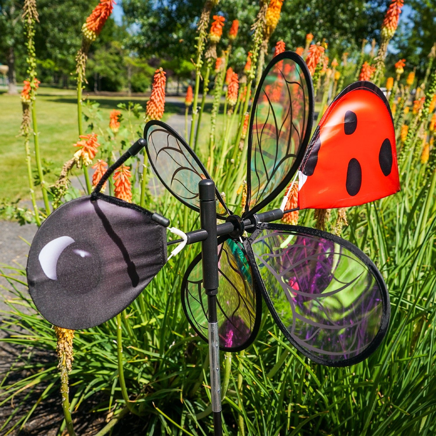 Pivoting Ladybug Spinner with vibrant design and iridescent petals spinning in a sunny garden setting, mounted on a sturdy pole.