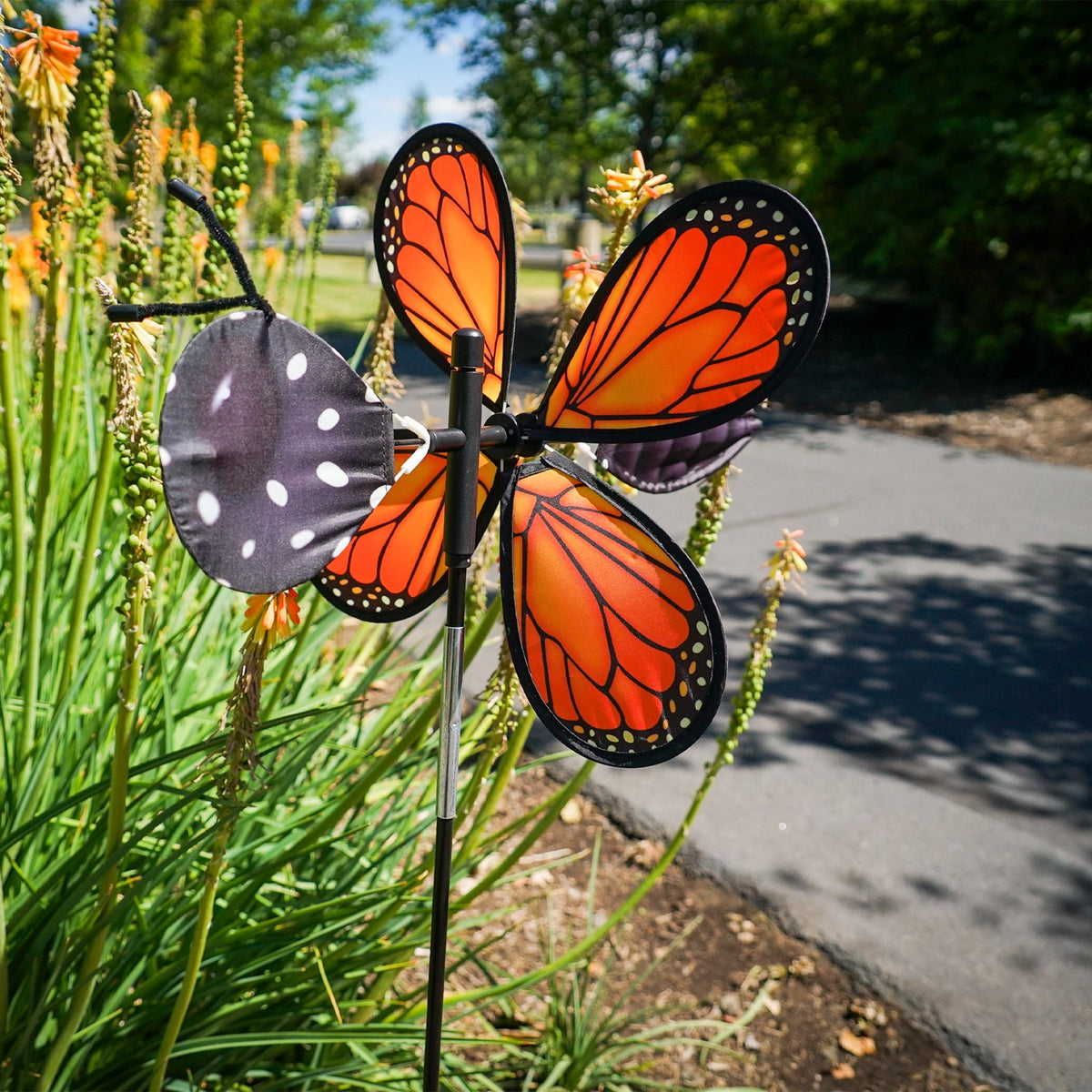 Vibrant Pivoting Monarch Butterfly Spinner in a garden, showcasing colorful petal design and fiberglass frame, adding motion to the outdoor space.