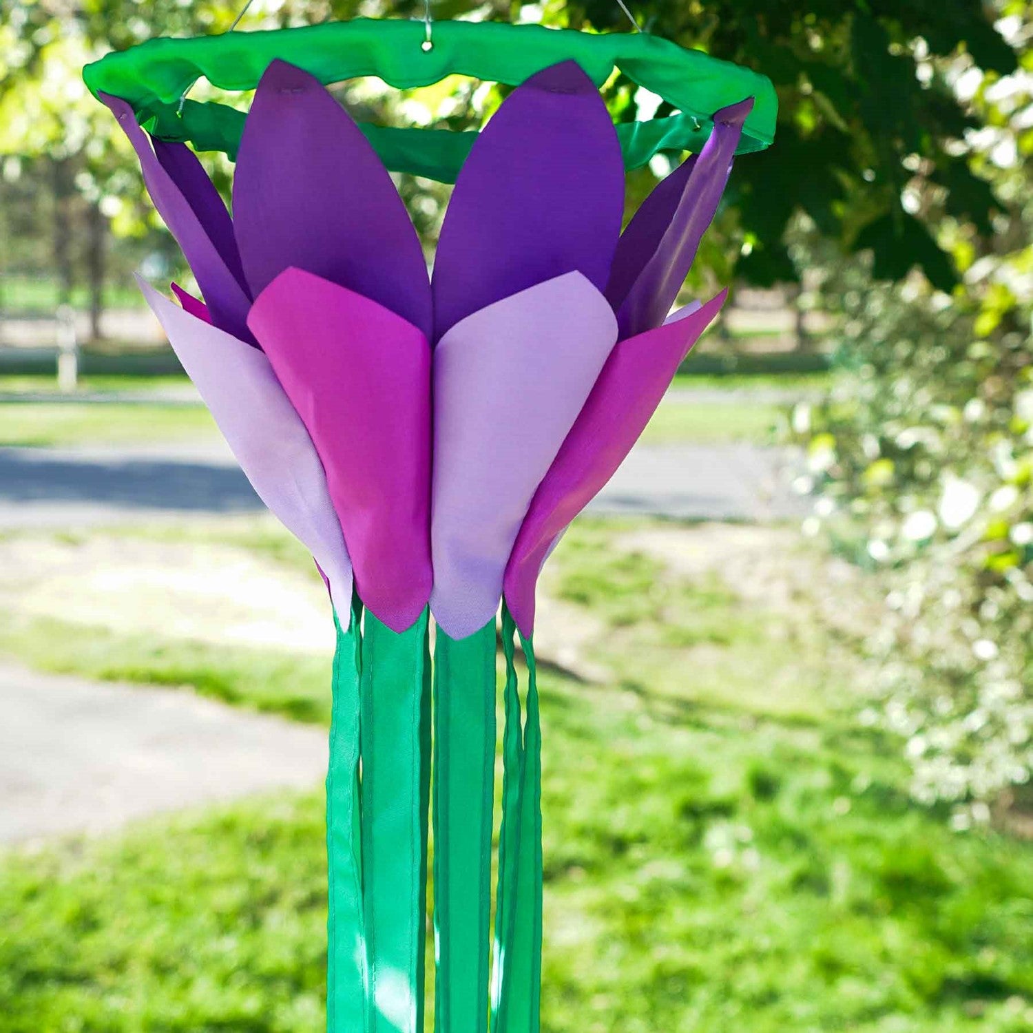 Purple 38 inch lotus flower windsock with bright petals and flowing green tails, elegantly displayed in a garden setting, showcasing its colorful design.