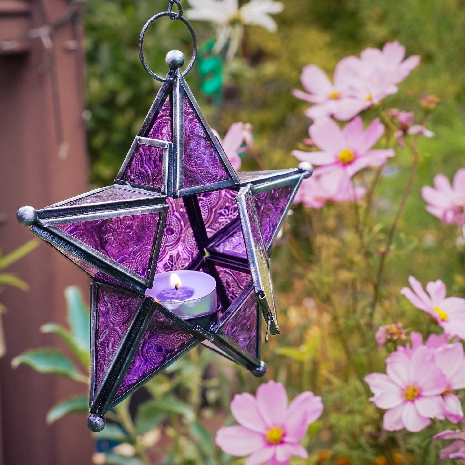 Purple 5-Point Star Hanging Tealight Lantern with intricate glass and metal design, hanging from a chain, creating a warm glow in a cozy setting.