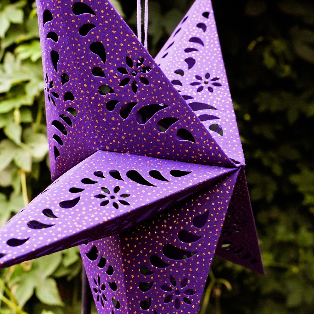 Purple Paper Star Lantern with intricate cutouts and gold accents, hanging indoors, illuminated with fairy lights for a cozy glow.