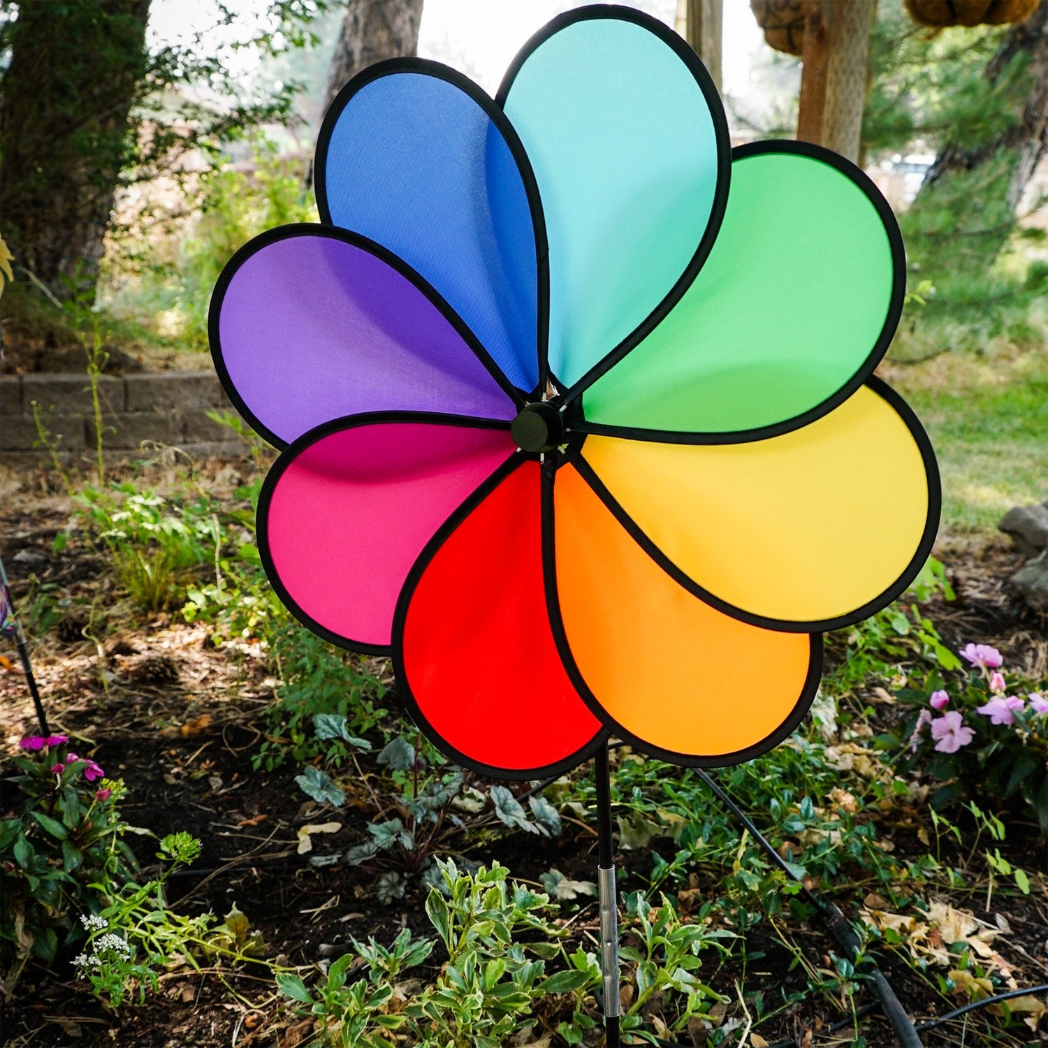 Rainbow Dazy Petal Spinner features eight colorful petals arranged in a flower design, spinning in the breeze atop a sturdy pole in a garden setting.