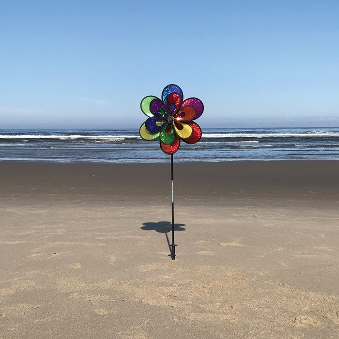 Rainbow Sparkle Windee Wheelz and Flower Spinner featuring double Mylar wheels adorned with colorful petals, spinning in a gentle breeze in a garden setting.