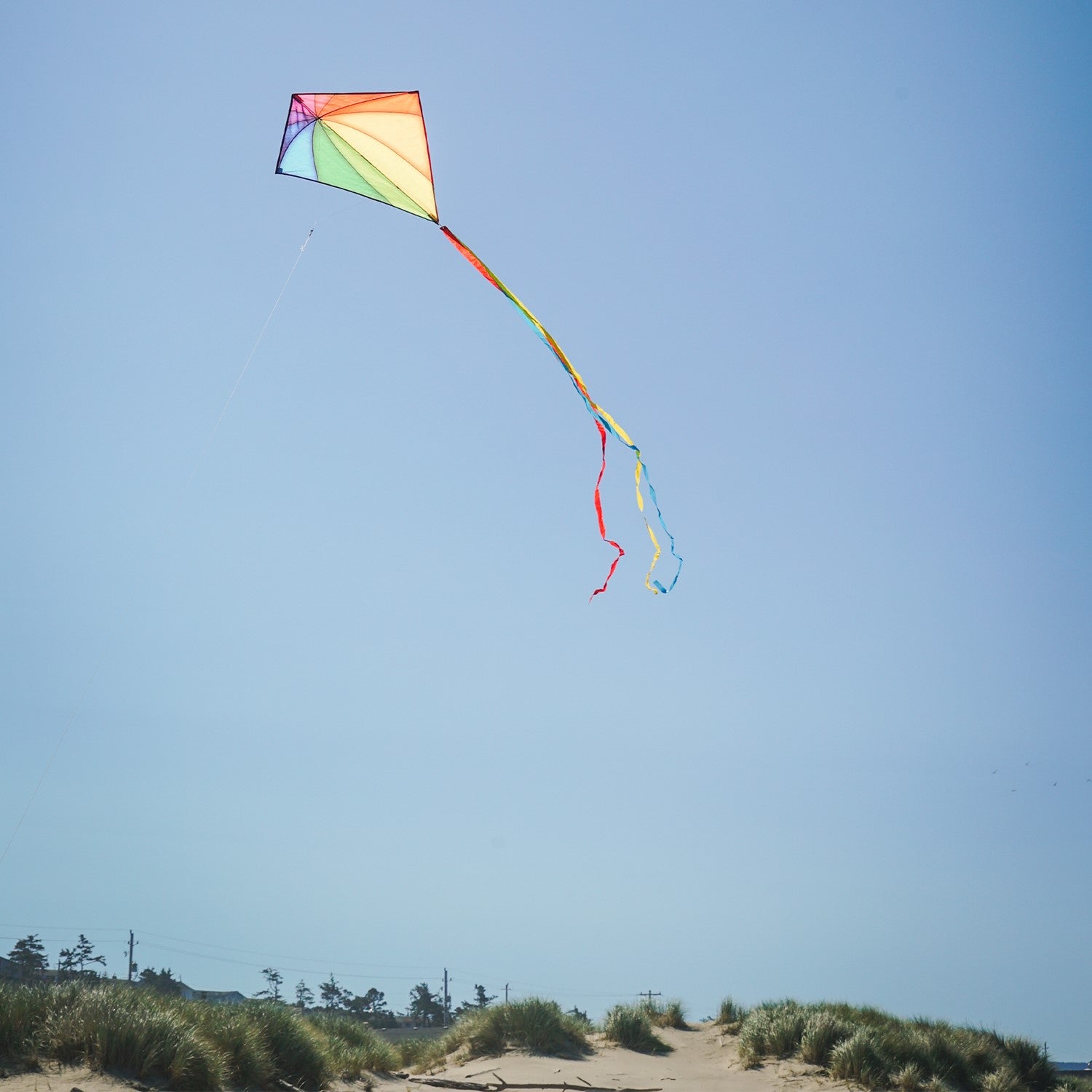 Colorful Rainbow Stained Glass 30-inch Diamond Kite flying against a blue sky, showcasing its vibrant stained glass patterns and attached tails.