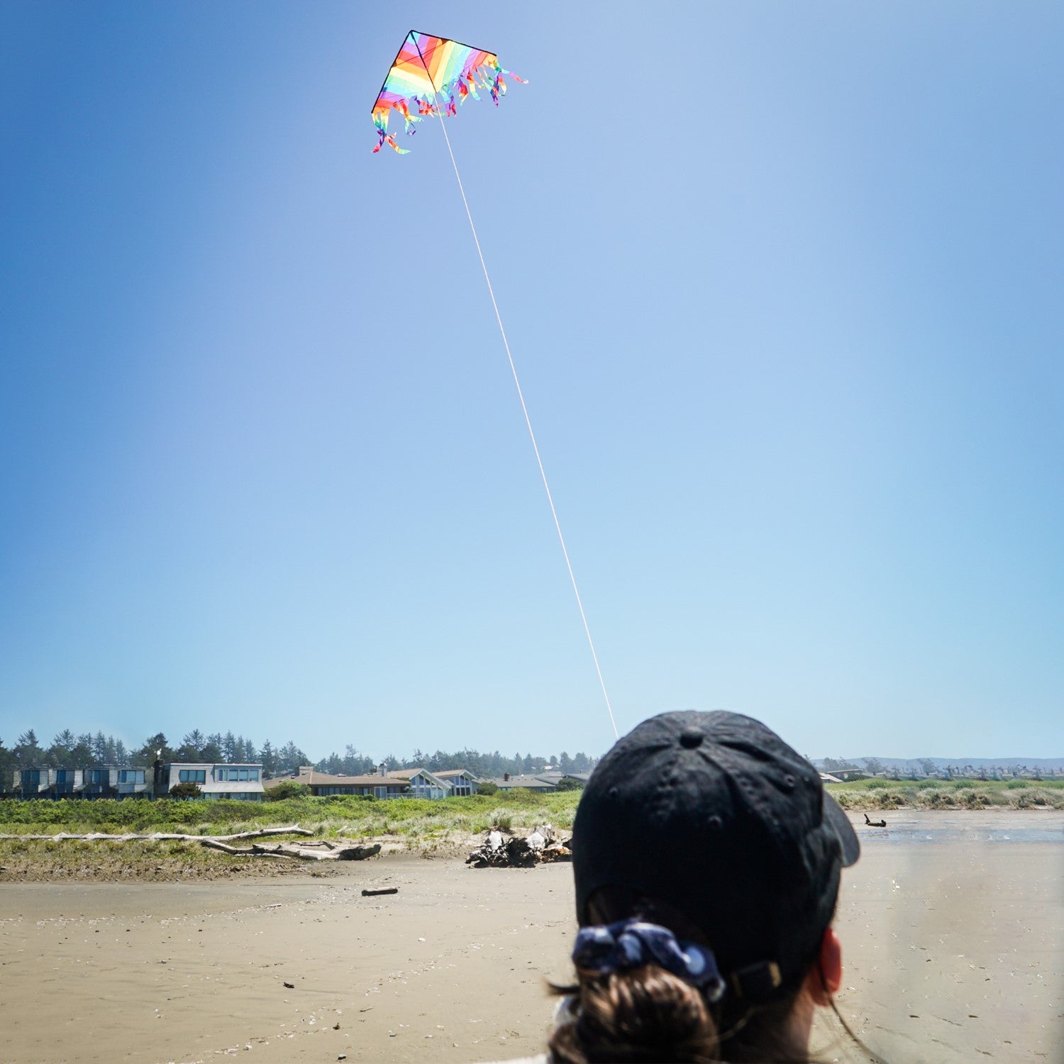 Rainbow Stripe 32' Flutterfly Delta Kite soaring high in the sky, showcasing vibrant colors and fluttering tails against a blue backdrop.