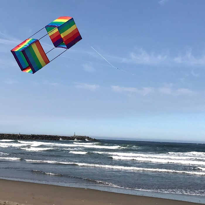 Rainbow Stripe Box Kite in mid-flight with colorful stripes against a clear blue sky, showcasing its vibrant 3D design.