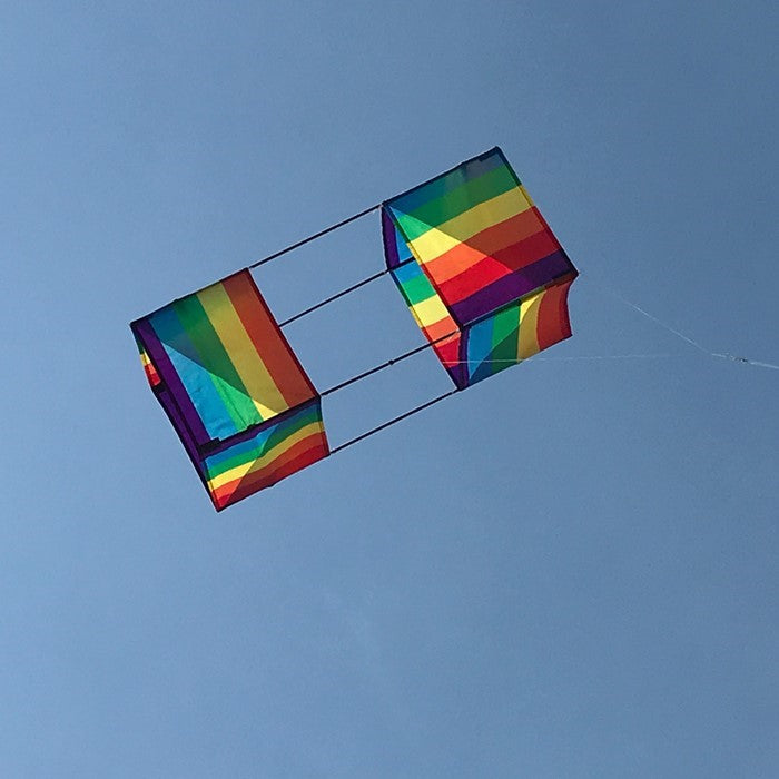 Rainbow Stripe Box Kite in mid-flight with colorful stripes against a clear blue sky, showcasing its vibrant 3D design.