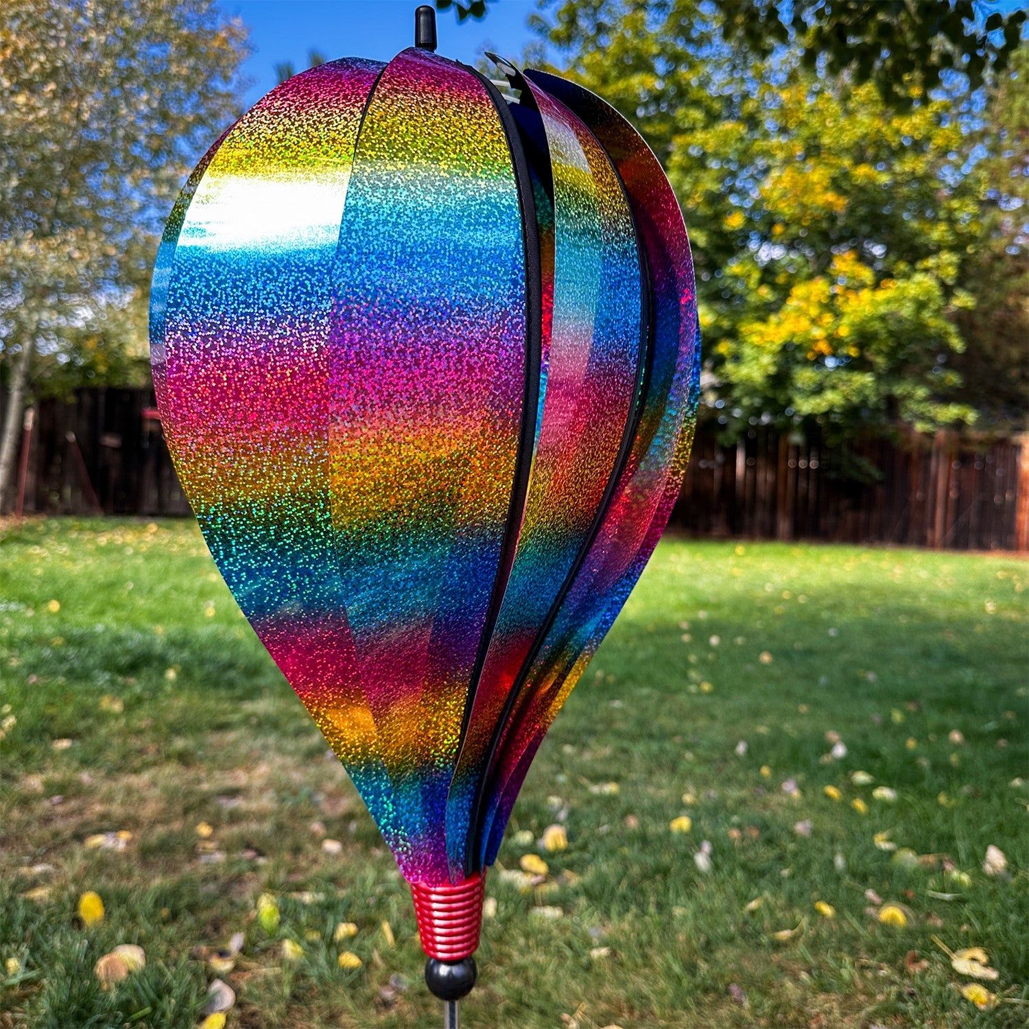 Rainbow Whirl 10-Panel Hot Air Balloon Ground Spinner with vibrant Mylar panels spinning gracefully in an outdoor garden setting.