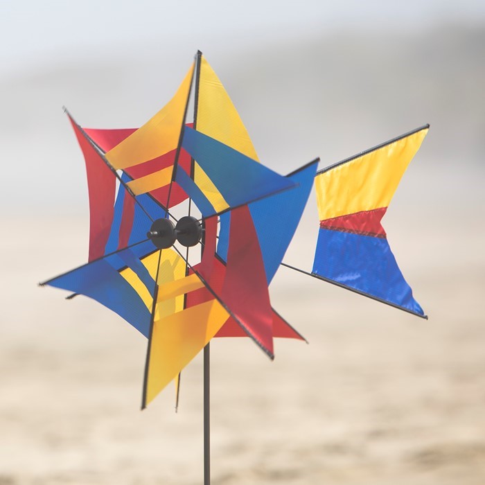 Red, Blue, and Yellow Kaleidoscope Ground Spinner elegantly incorporates a kaleidoscope sail design that spins with the wind, perfect for garden display.