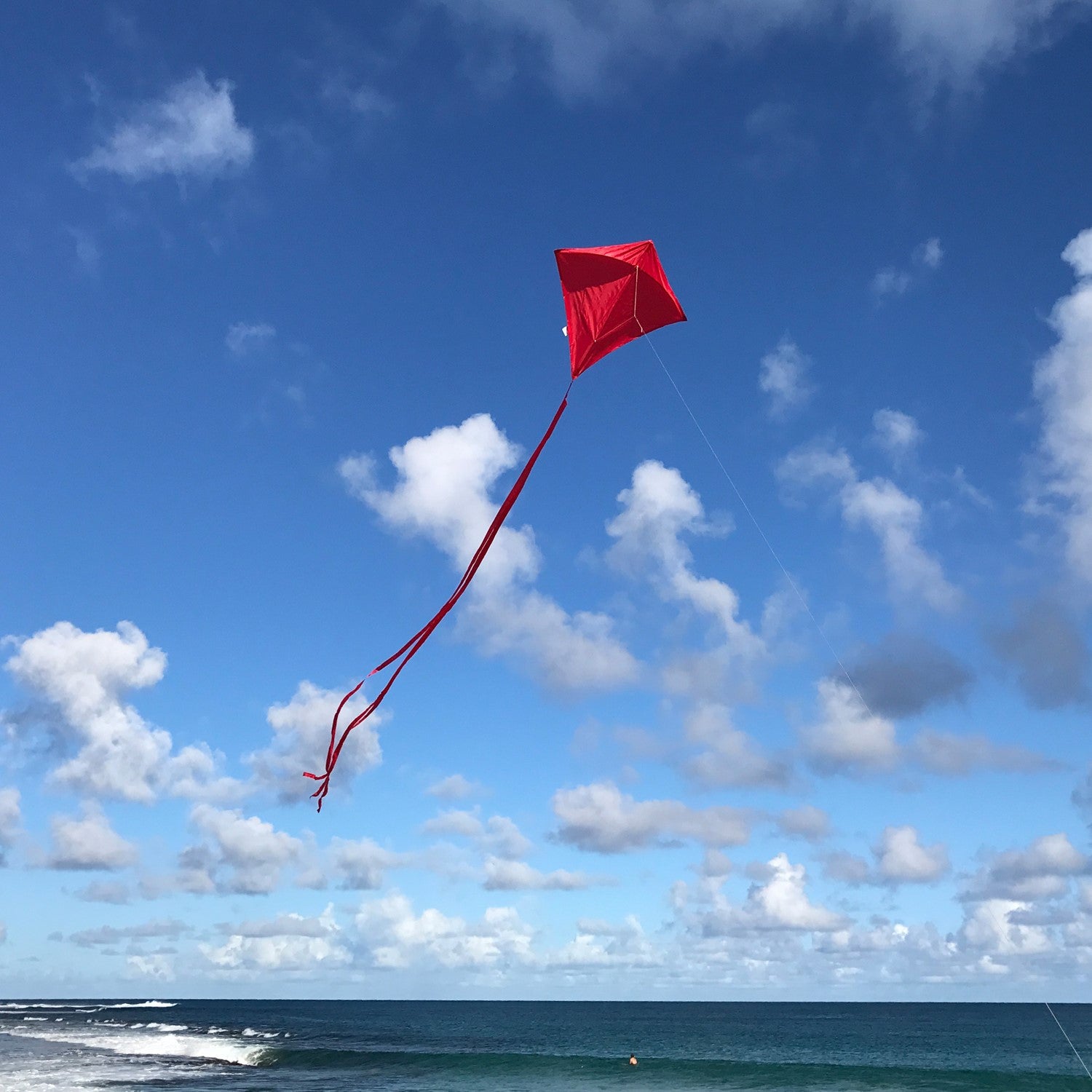 Red Colorfly 30\" Diamond Kite soaring with three colorful tails against a clear blue sky, showcasing its durable design and vibrant color.