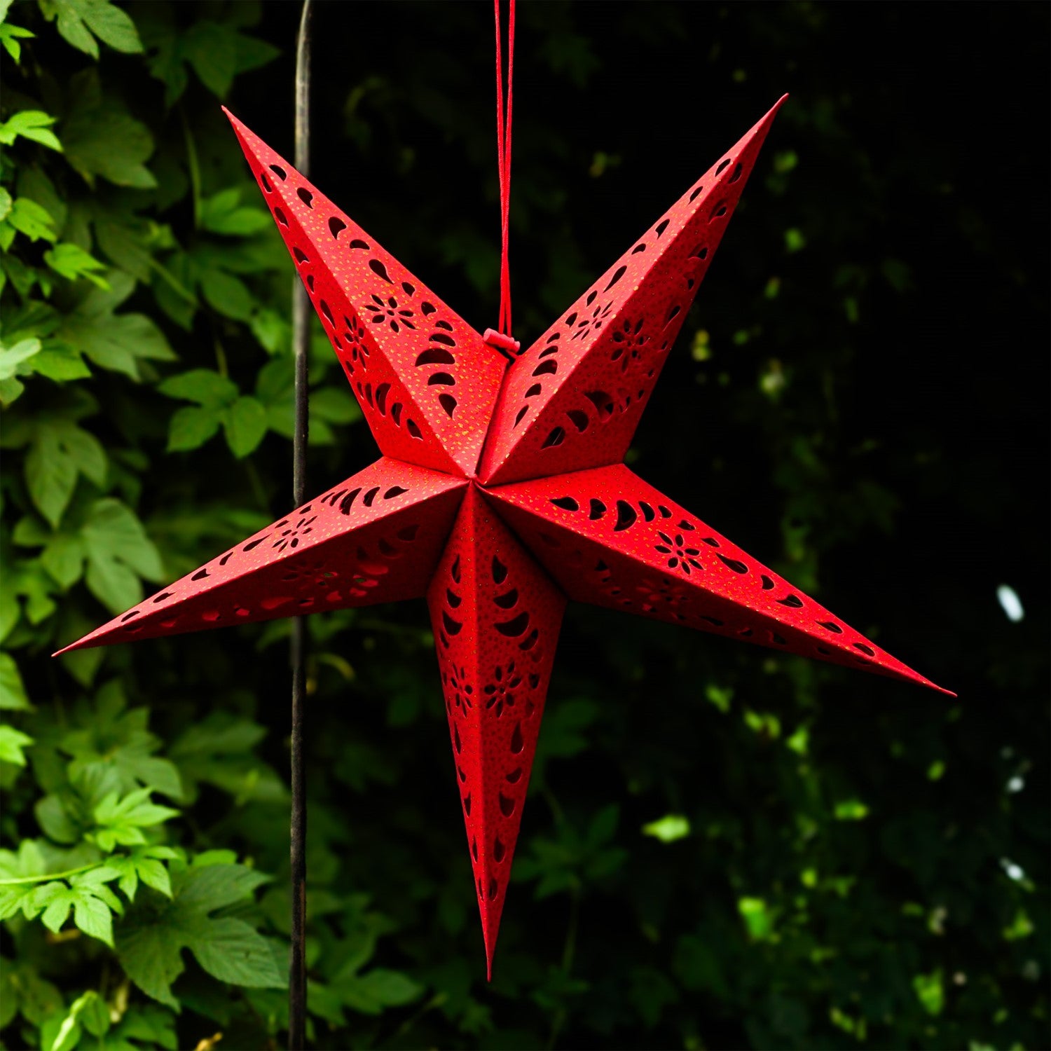 A Red Paper Star Lantern with intricate cutouts, elegantly hanging and illuminated, showcasing its vibrant color and gold accents in warm light.