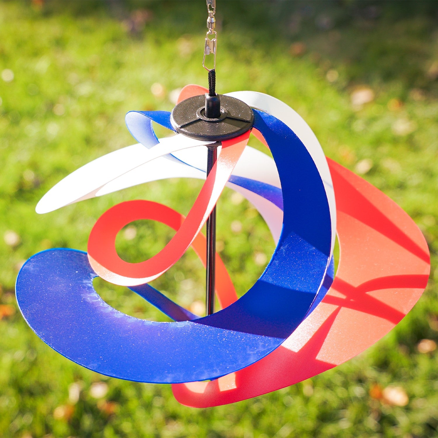 Red, White and Blue Poly Vortex Spinner with interconnected spirals in motion, hanging outdoors amidst greenery, showcasing vibrant colors and patriotic spirit.