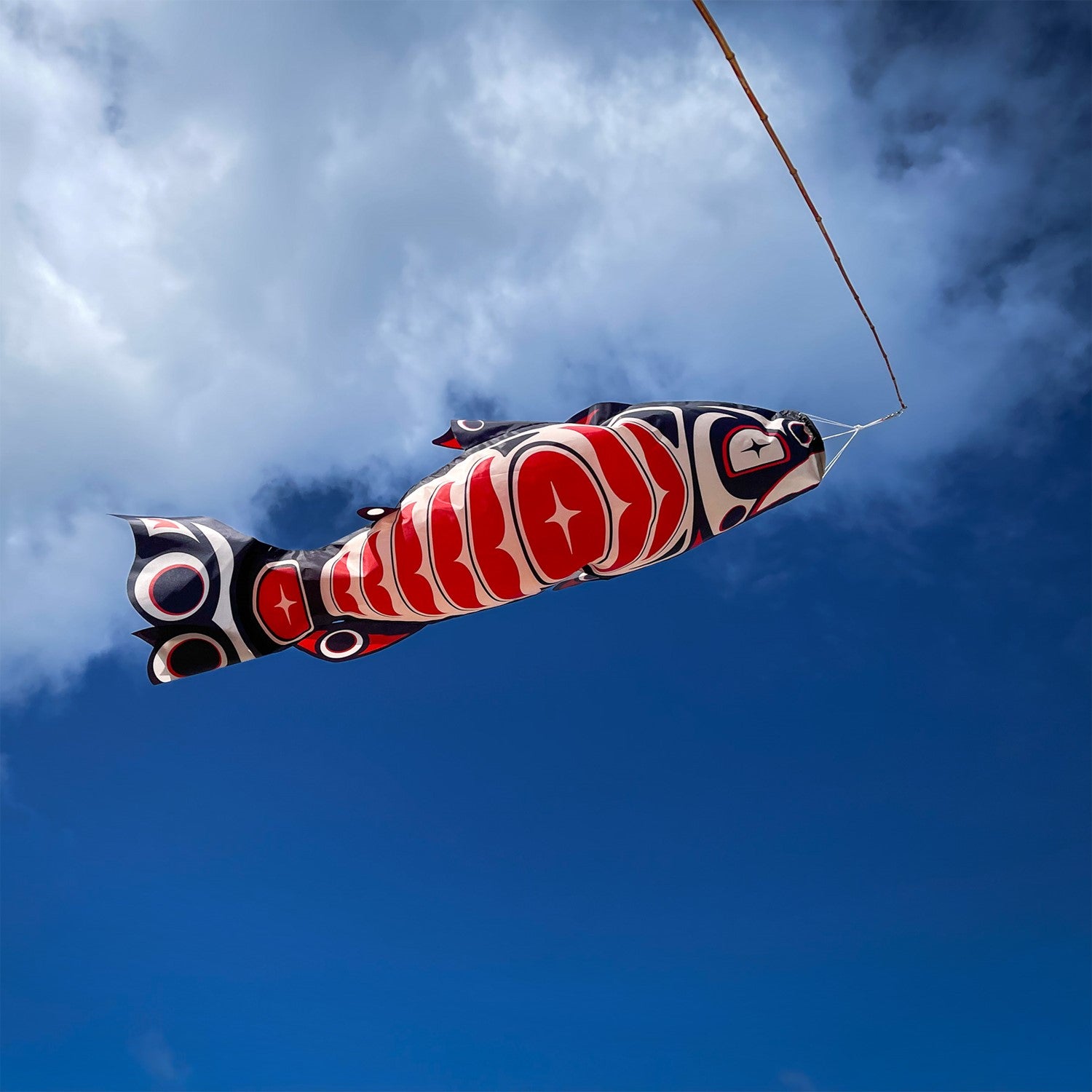 Salmon Totem 48' Fish Windsock featuring vibrant printed patterns hanging outdoors, gently fluttering in the breeze.