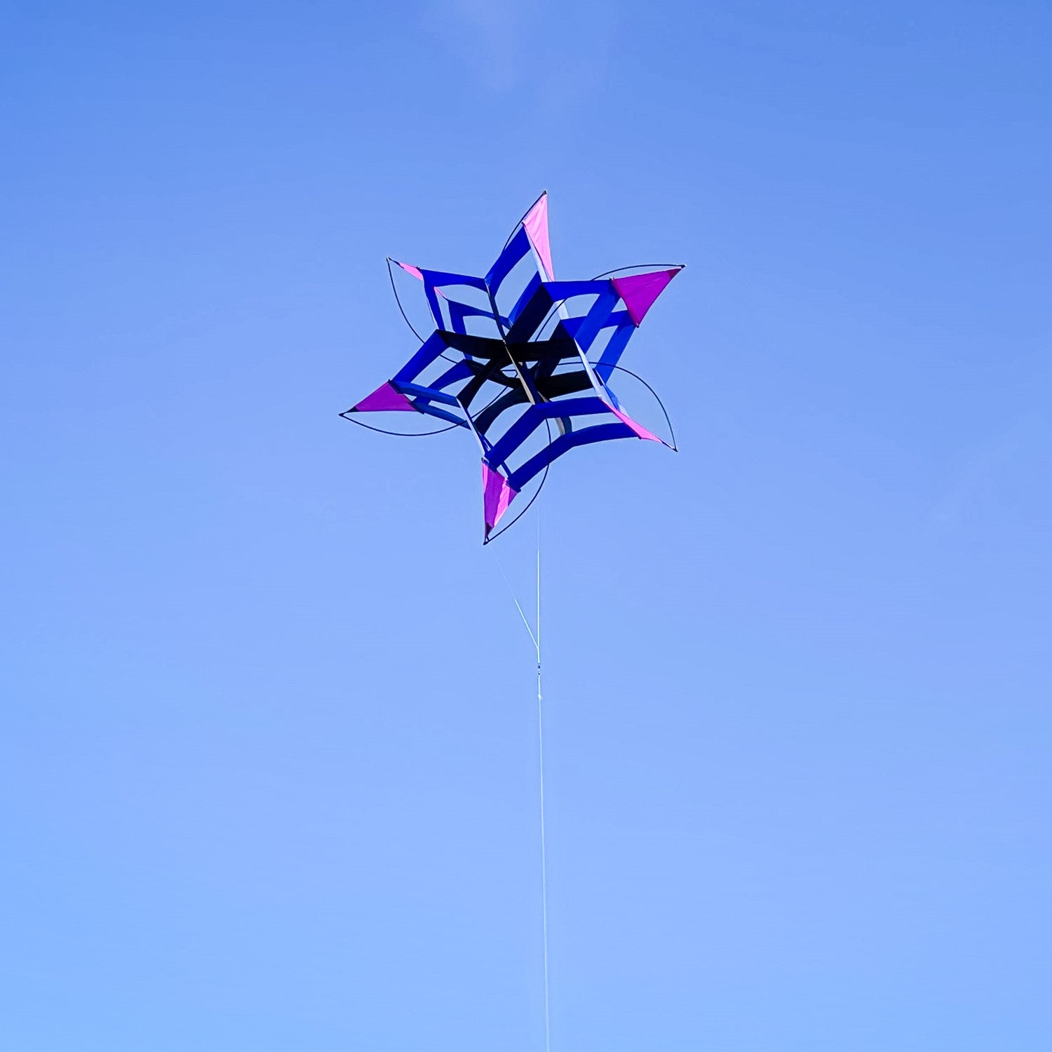 Shadow Cosmic Hex Kite soaring against a blue sky, showcasing its colorful design and cellular structure.