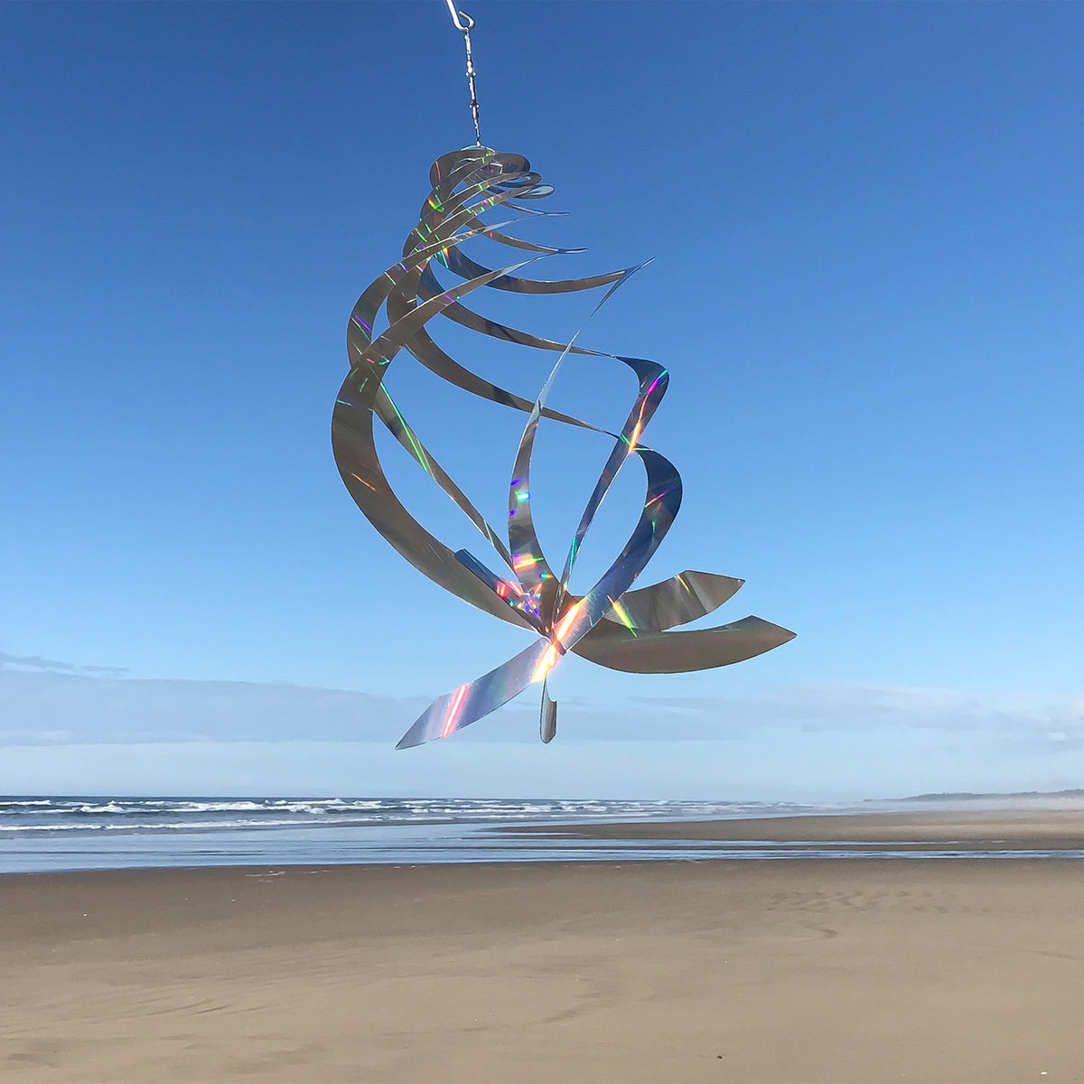 Sheen Crystal Spinner made of holographic Mylar, featuring five spinning blades reflecting rainbow colors, hanging in a garden with sunlight.