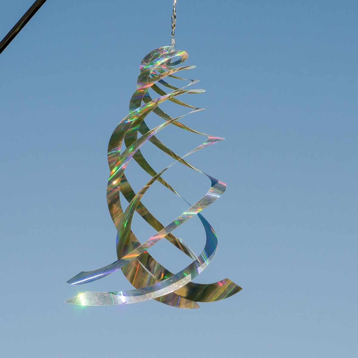 Sheen Crystal Spinner made of holographic Mylar, featuring five spinning blades reflecting rainbow colors, hanging in a garden with sunlight.