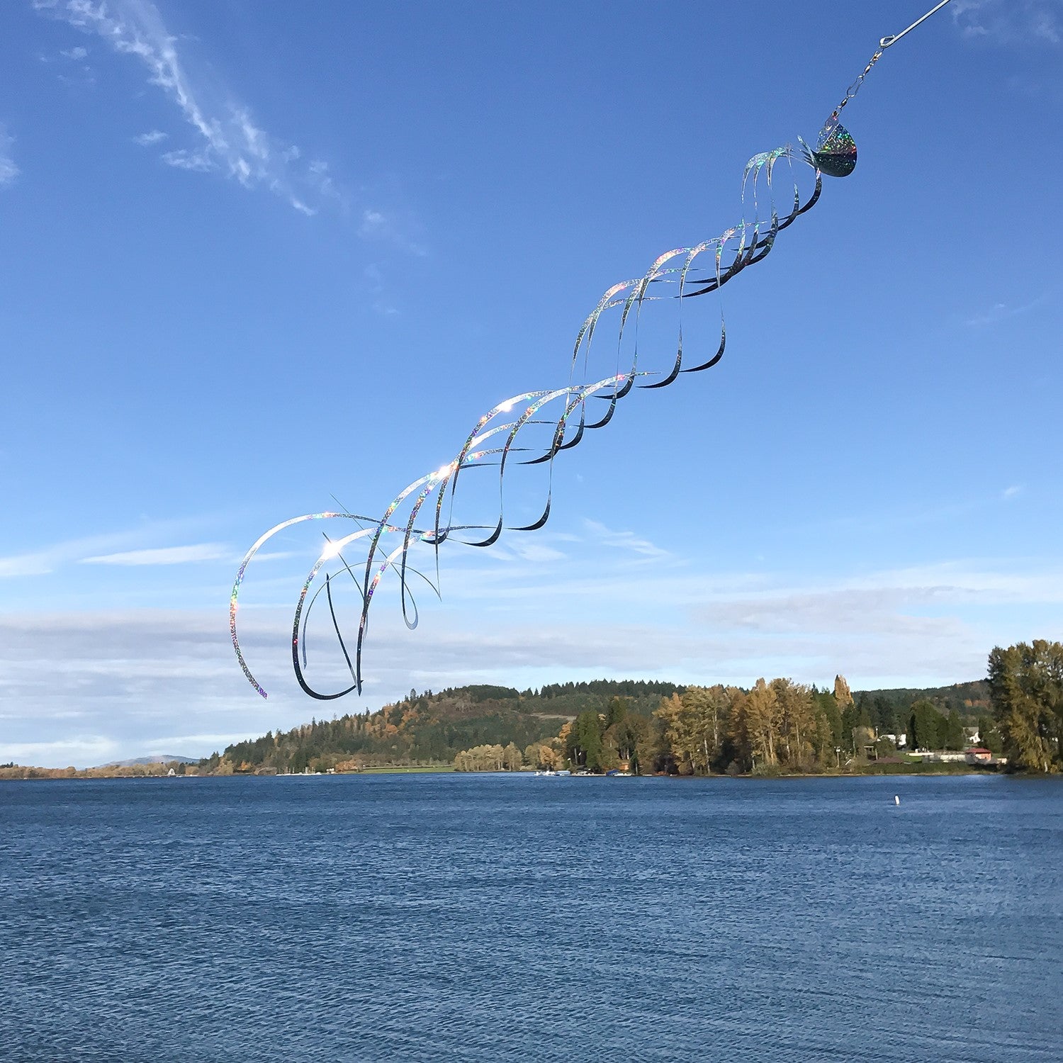 Silver Mylar Turbulence Spinner in a garden setting, showcasing its reflective surface and curlie design while spinning in the wind.