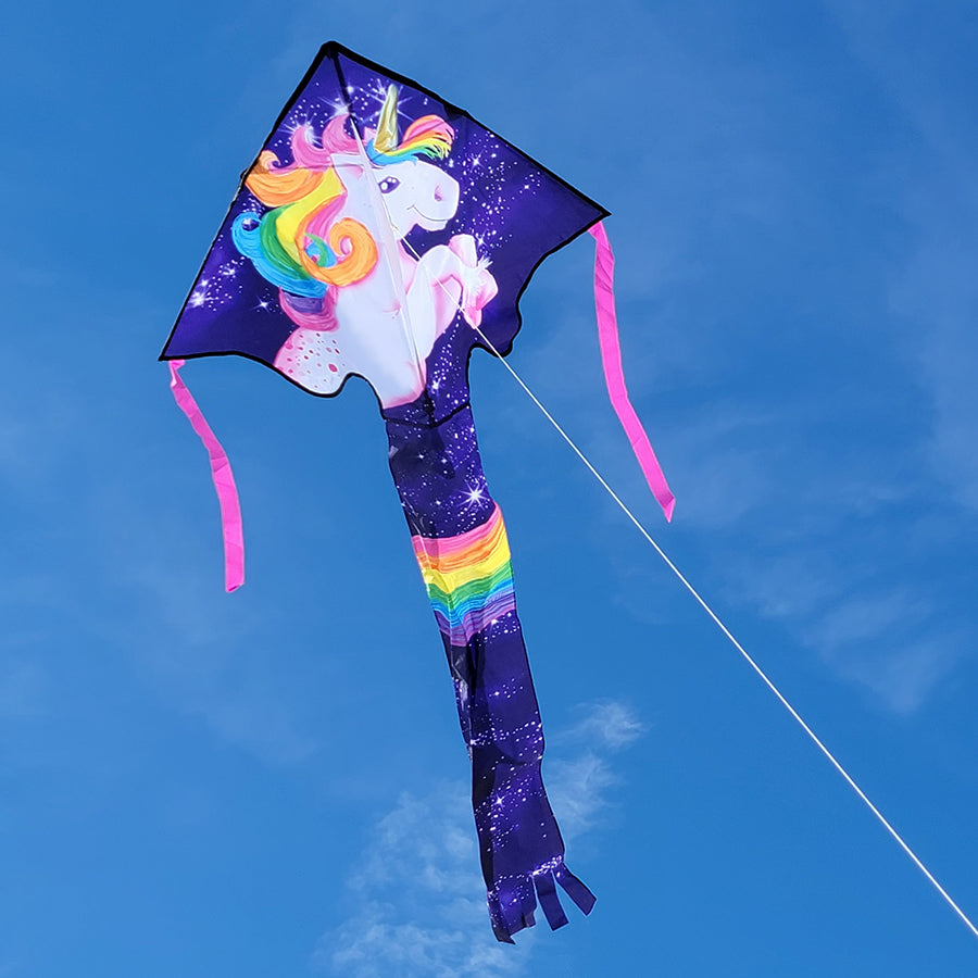 Super Flier Kite in vibrant unicorn design, measuring 46x90 inches, soaring against a clear blue sky at a beach.