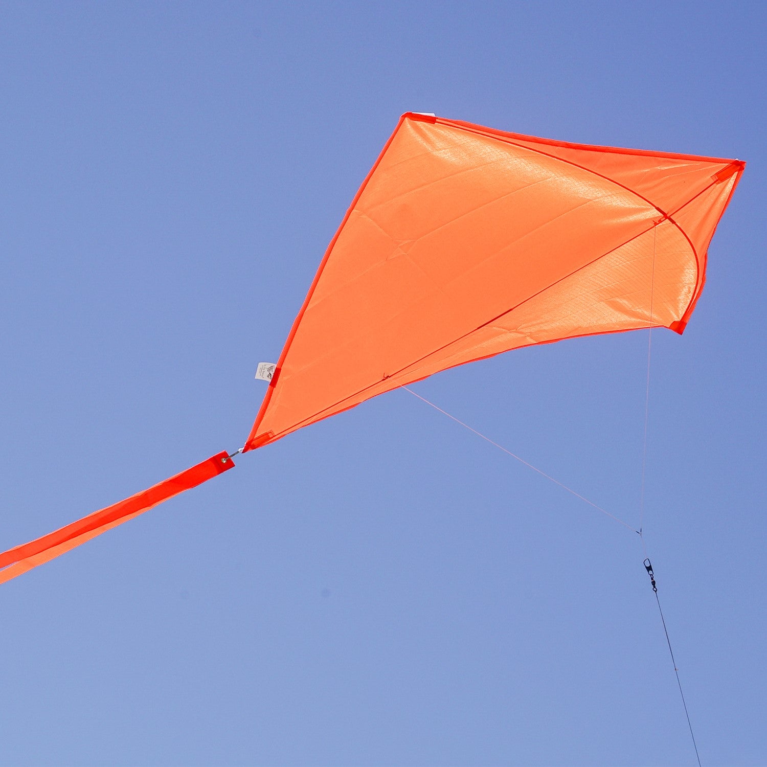 Tangerine Colorfly 30-inch diamond kite soaring against a blue sky, featuring three colorful tails and a lightweight design for easy flying.