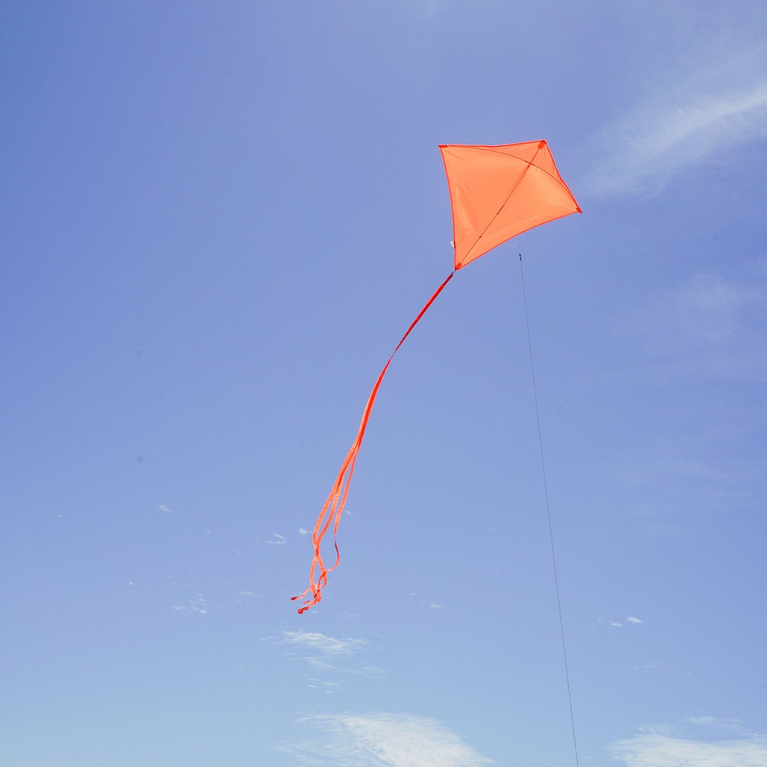 Tangerine Colorfly 30-inch diamond kite soaring against a blue sky, featuring three colorful tails and a lightweight design for easy flying.
