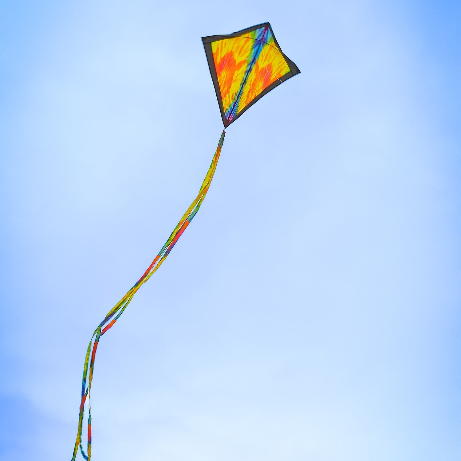 Tie Dye 30 inch Diamond Kite flying high in the sky with vibrant colors and 12-foot streamer tails swaying in the wind.