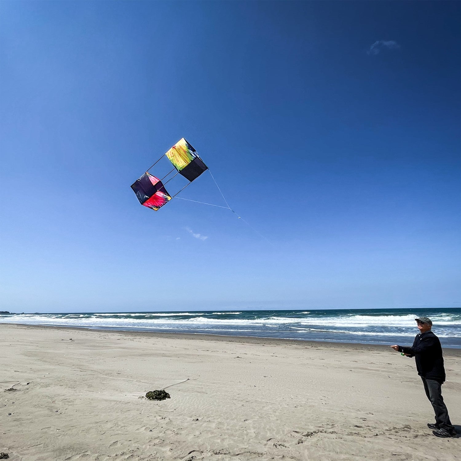 Tie Dye Box Kite flying high against a blue sky, showcasing its vibrant tie-dye design and sturdy fiberglass structure.