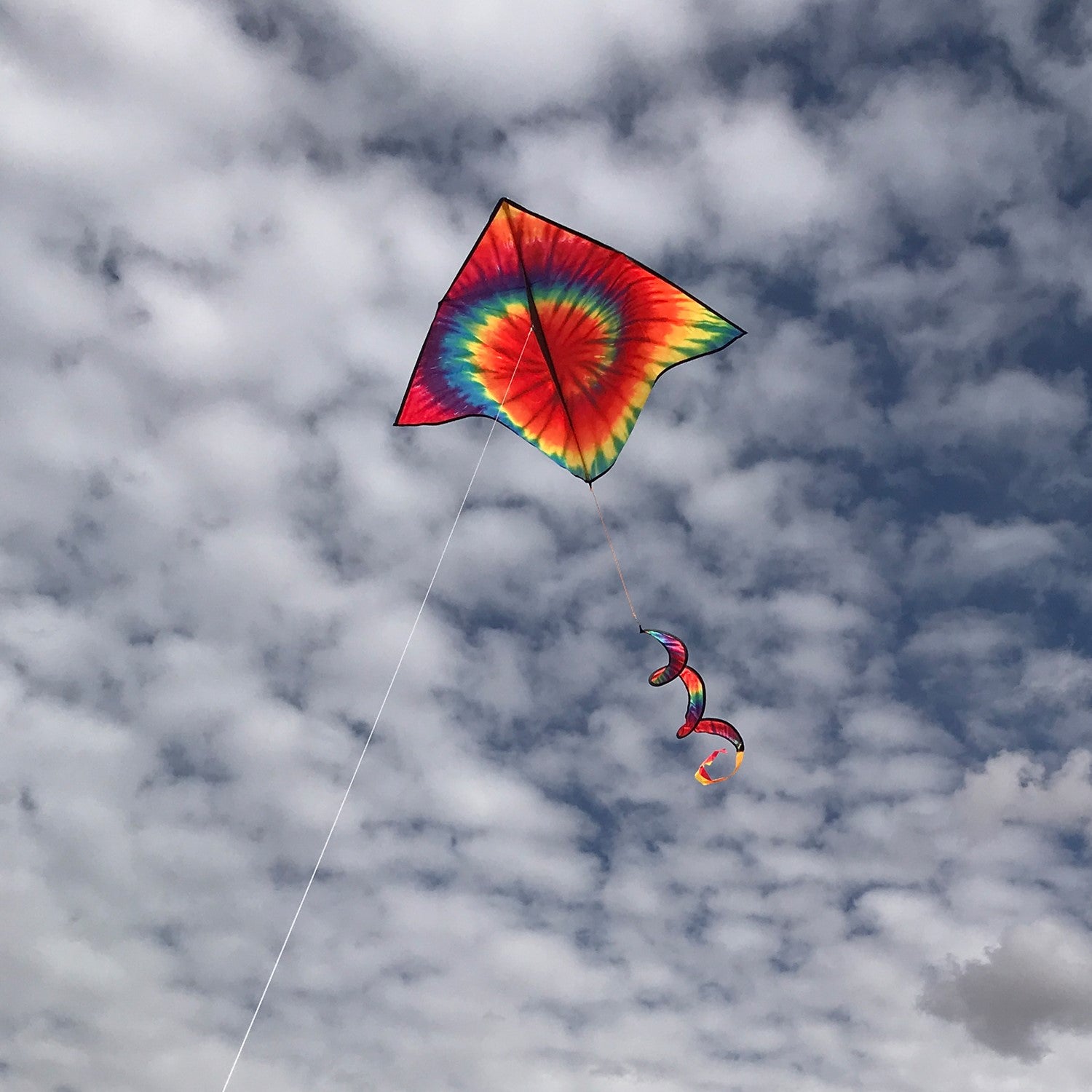 Tie Dye Delta with Spinning Tail flying in a clear blue sky, showcasing vibrant rainbow colors and a matching spinner tail.