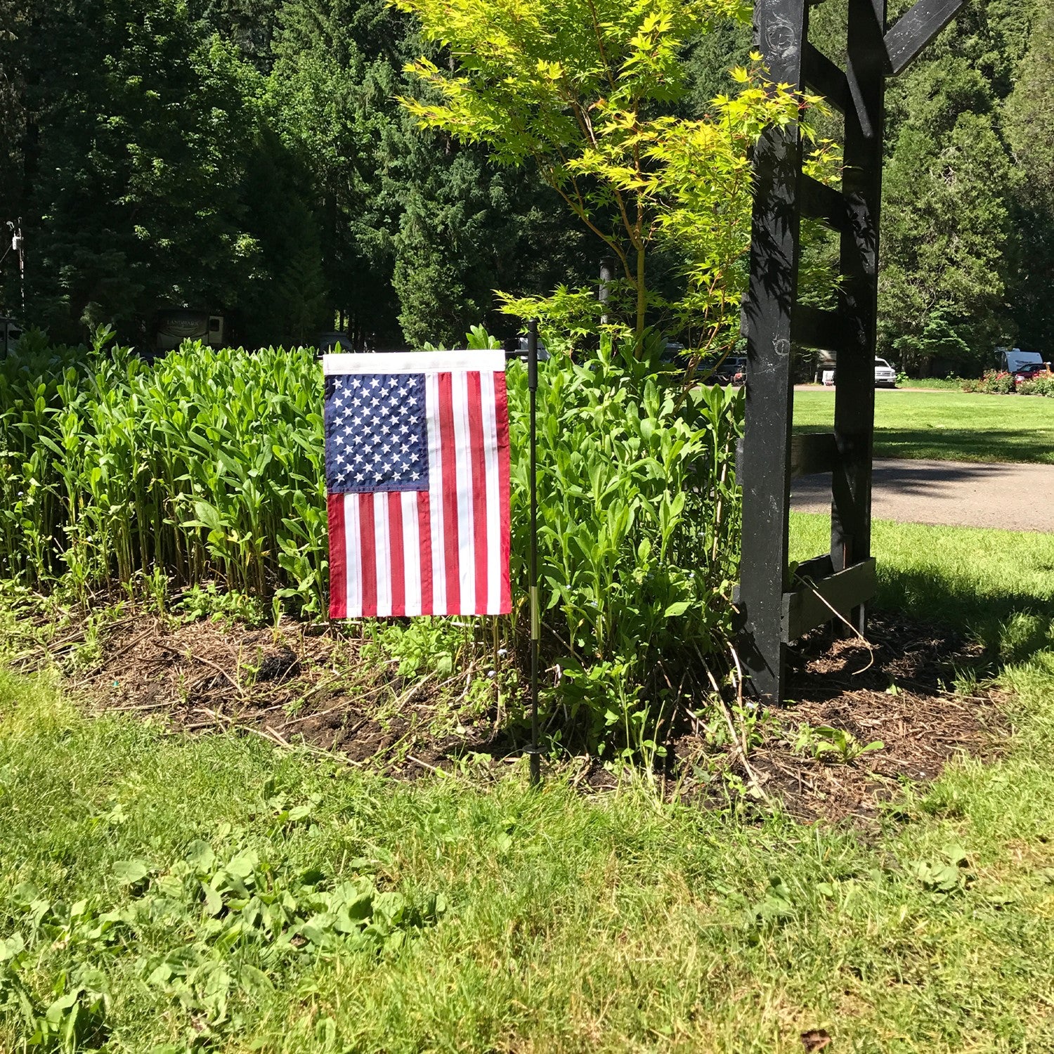 US Flag Embroidered Garden Flag with embroidered stars displayed on a flagpole in a vibrant garden setting.