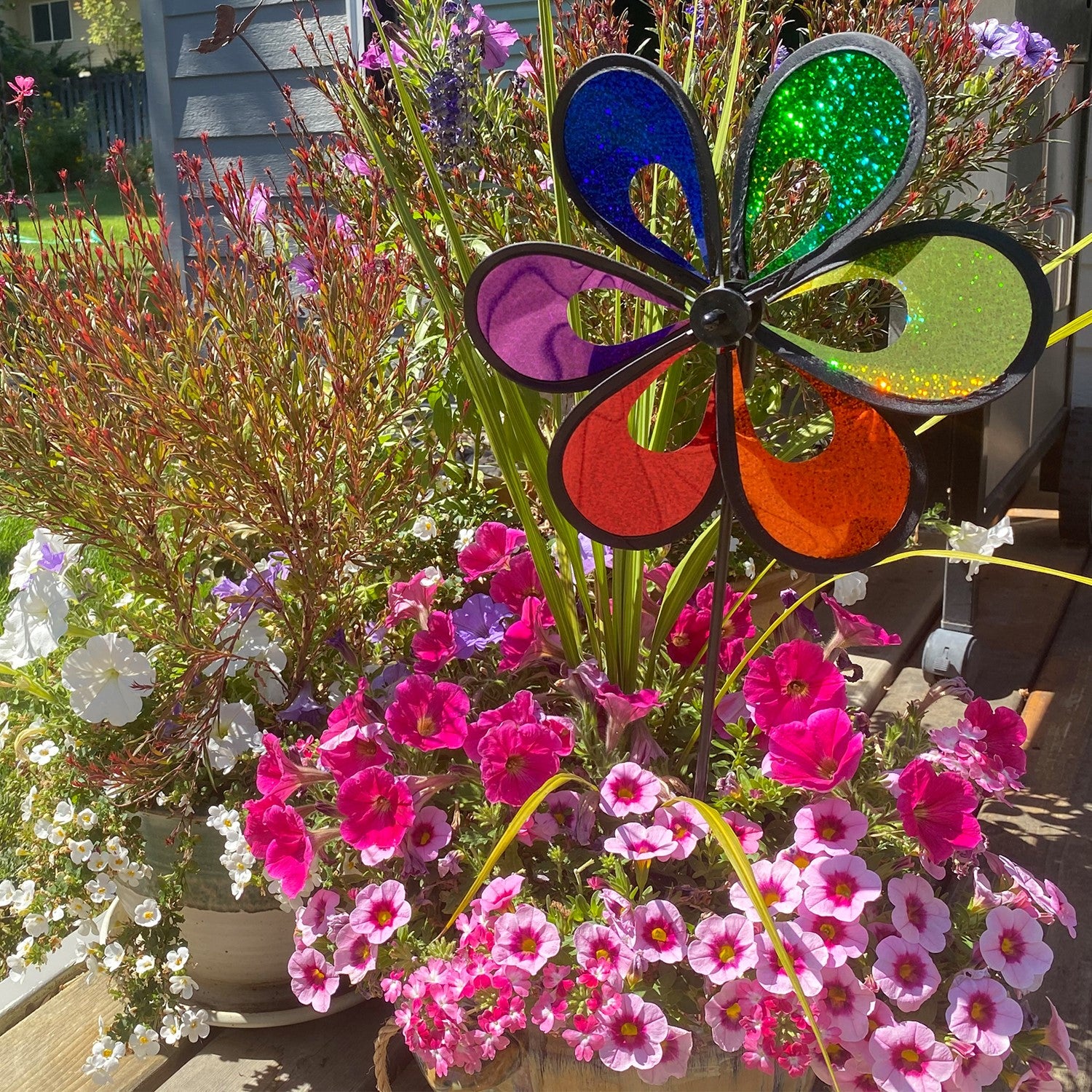 10-inch Rainbow Mylar Windee Wheelz Spinner with colorful petals, spinning atop a 17-inch fiberglass pole in a garden setting.