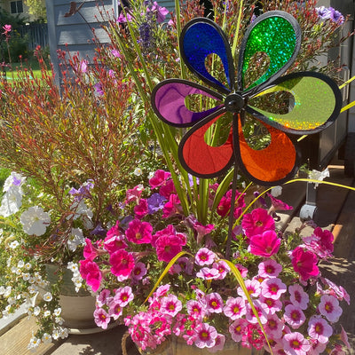 10-inch Rainbow Mylar Windee Wheelz Spinner with colorful petals, spinning atop a 17-inch fiberglass pole in a garden setting.