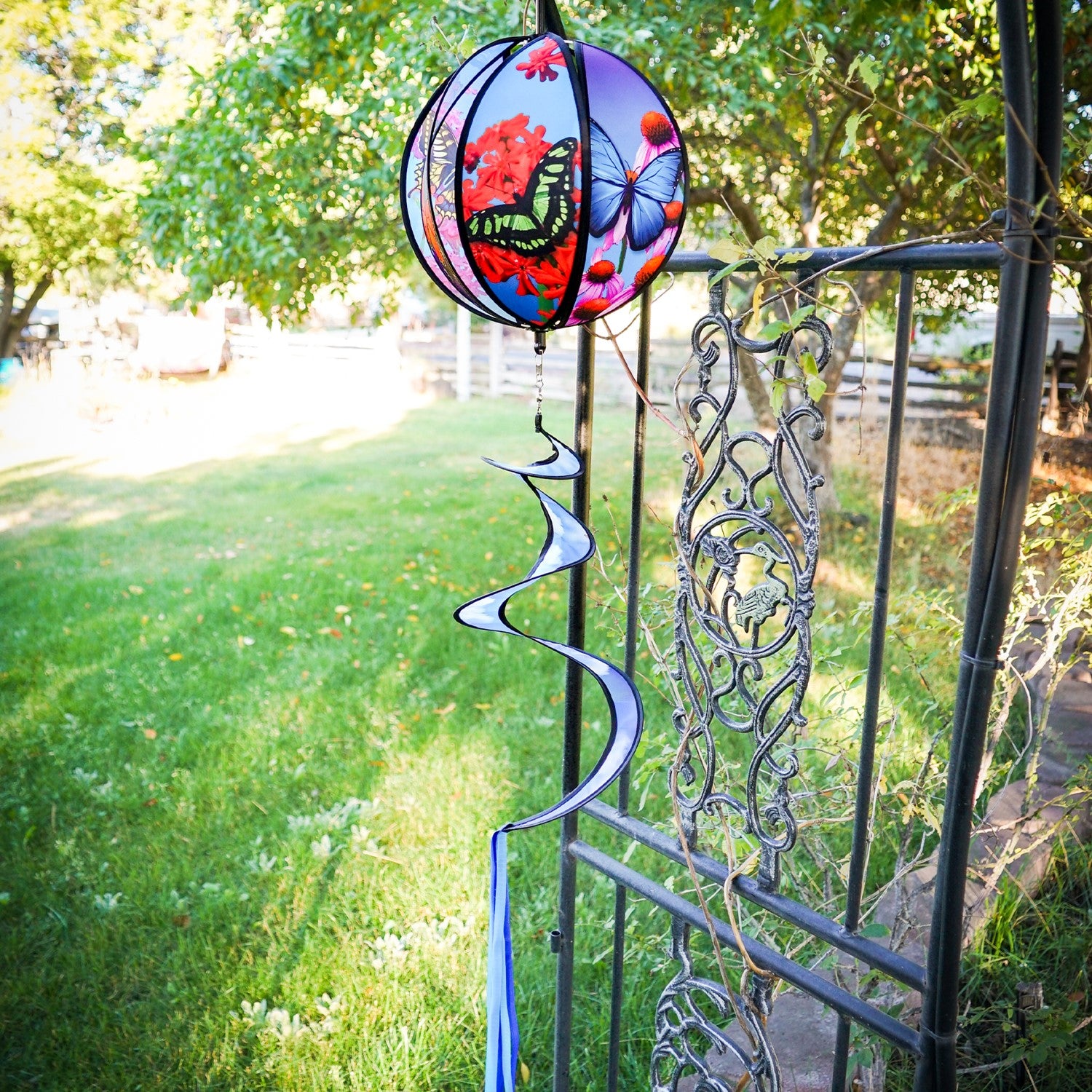 11-inch butterfly hanging ball spinner with six colorful butterfly design panels spinning in a garden setting on a sunny day.