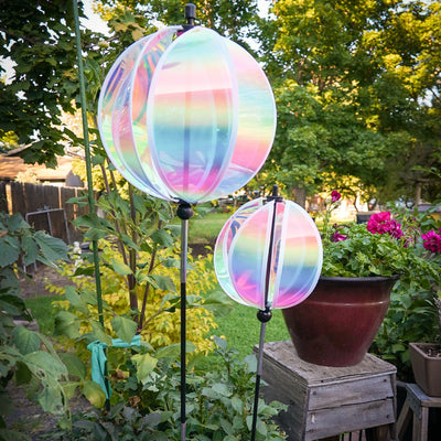 An 11" striped iridescent gazing ball displayed in a garden, featuring colorful reflections and a durable pole for stability.