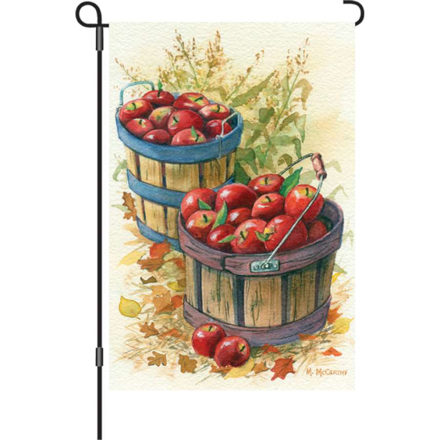 Illuminated 12 in. Apple Baskets garden flag displaying vibrant colors, featuring a cozy autumn theme in a well-maintained garden setting.