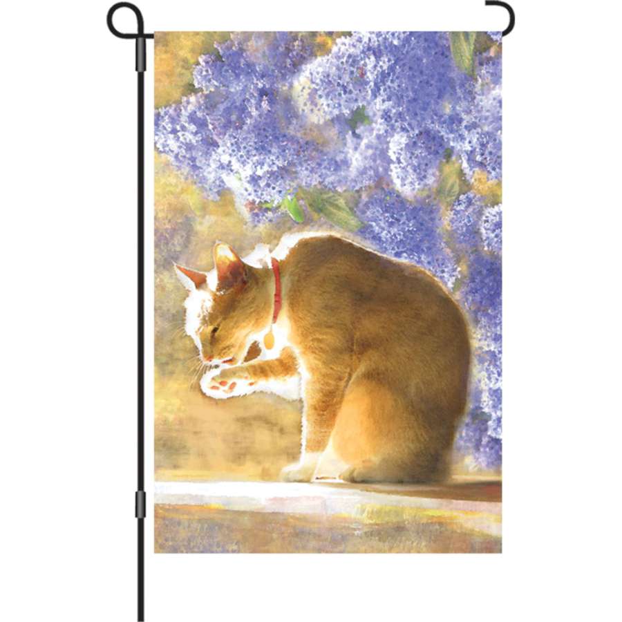 Illuminated 12 in. Bathing Tabby garden flag featuring a playful tabby cat design displayed on an outdoor flag stand in a bright garden setting.