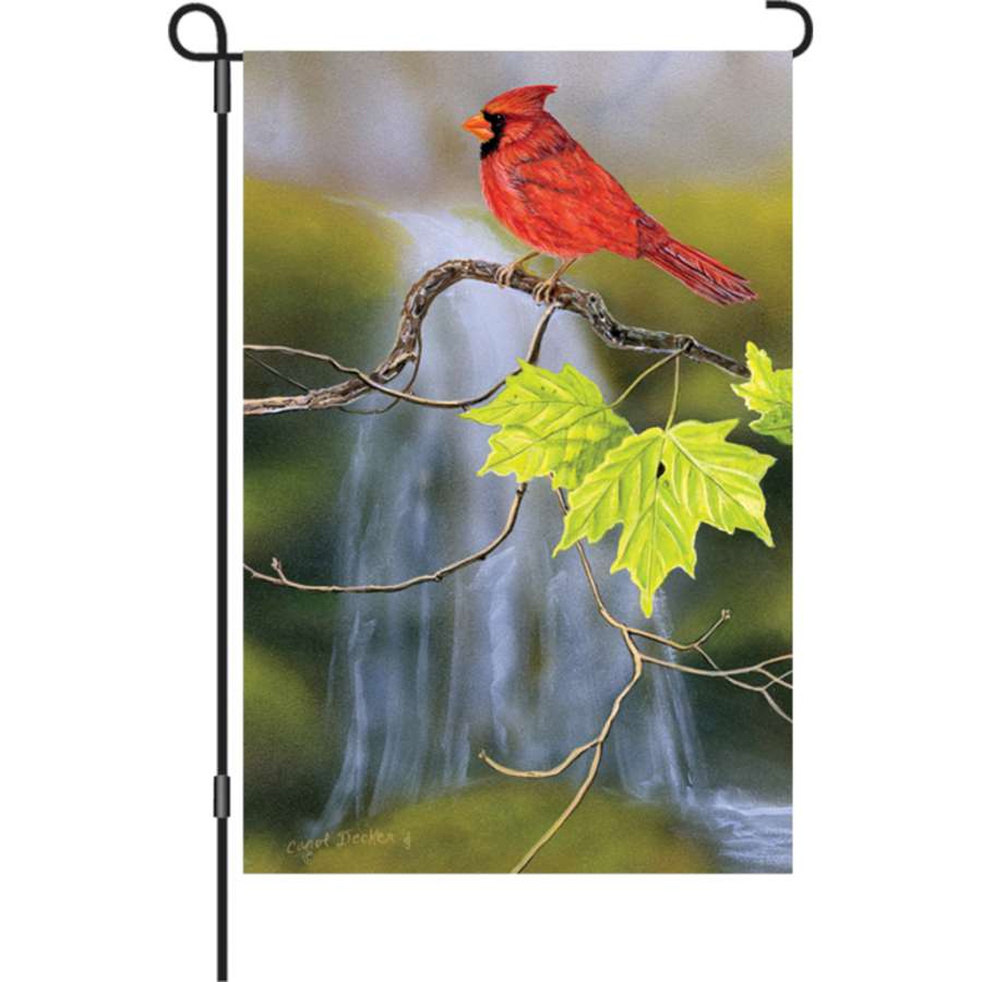 Illuminated 12 in. garden flag featuring a cardinal and waterfall design, displayed outdoors in a garden setting with colorful flowers.