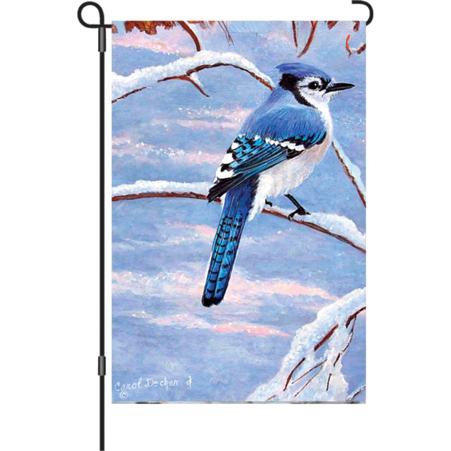 12 in. Winter Blue Jay garden flag illuminated with vivid colors hanging on a decorative flag pole in a flower bed.