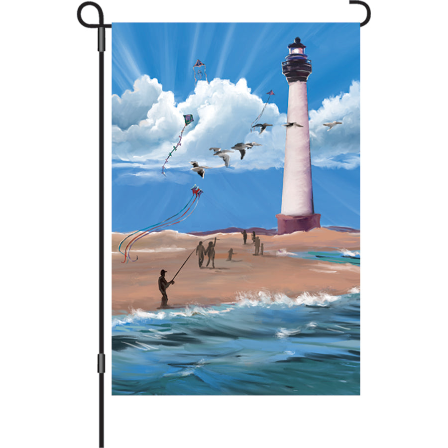 12 in. Lighthouse Breezy Day garden flag featuring an illuminated coastal scene, displayed outdoors, enhancing the charm of the garden.