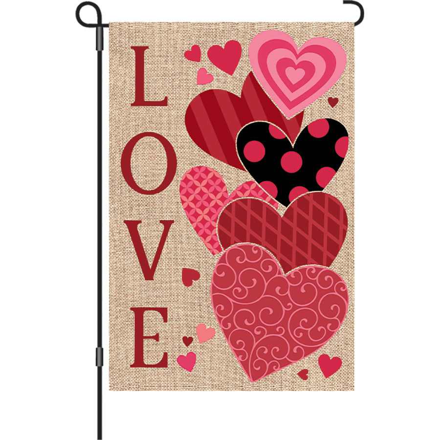12 in. Love Hearts garden flag featuring colorful hearts and the word 'LOVE' displayed on a garden pole in a sunny outdoor setting.