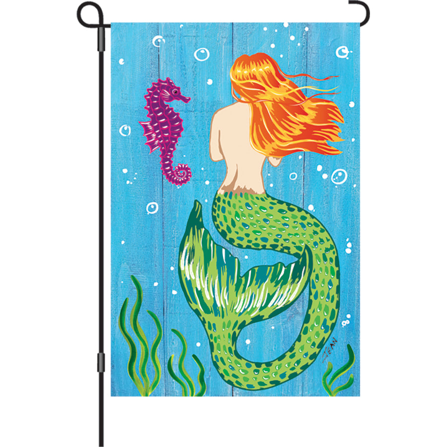 12 in. Mermaid & Seahorse garden flag showcasing whimsical marine designs, displayed in a garden setting swaying in the breeze.
