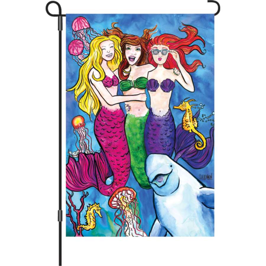 A colorful 12-inch #Mermaidsquad flag featuring a whimsical mermaid design, displayed outdoors in a sunny garden setting.