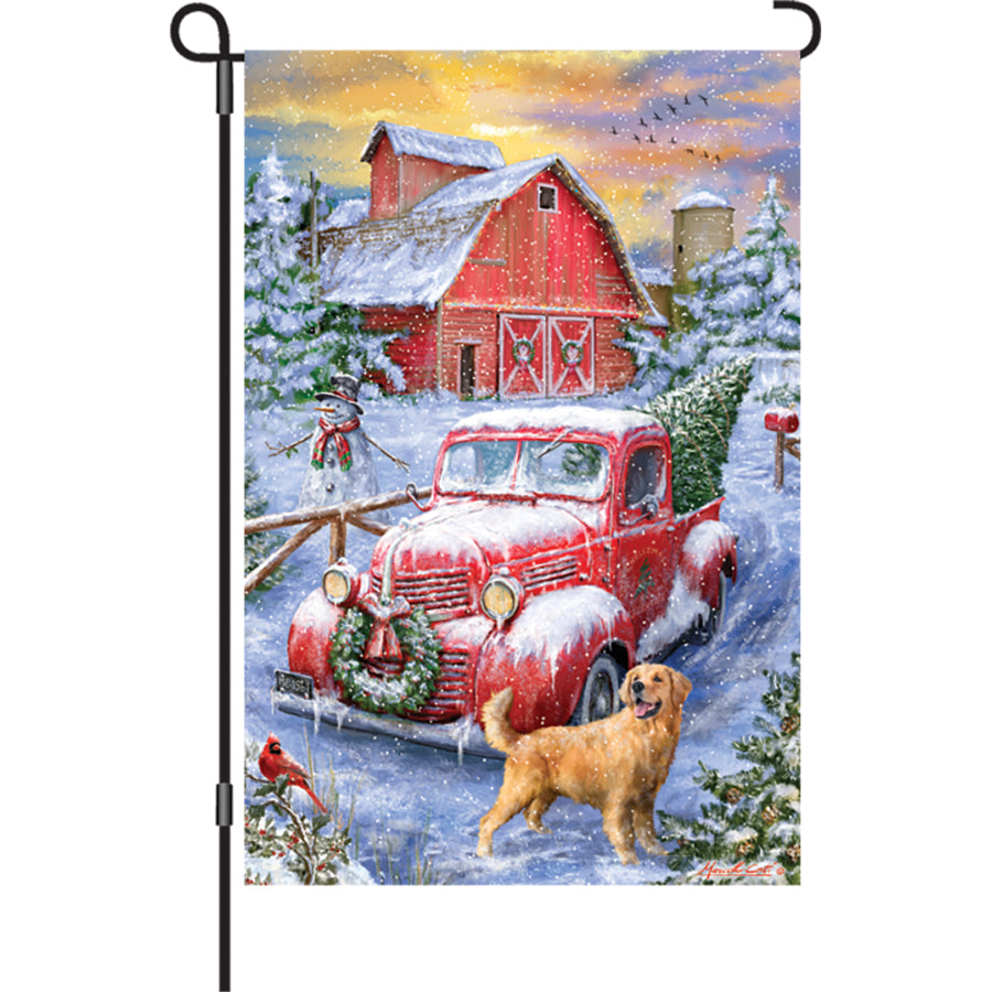 12 in. Red Truck Winter garden flag, depicting a cheerful red truck with winter accents, displayed in an outdoor garden setting.