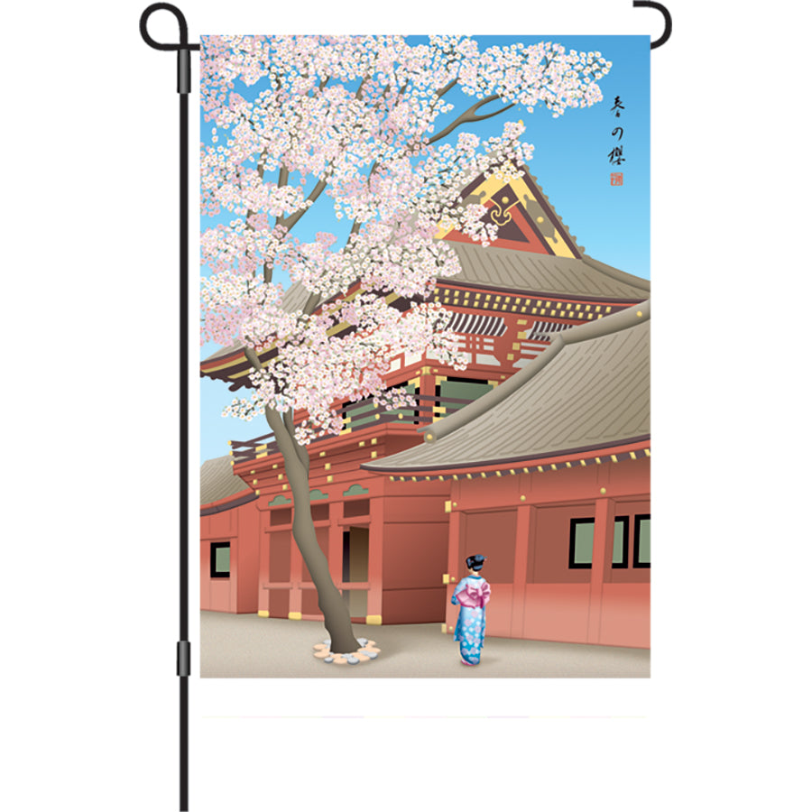 12 in. Sakura In Bloom garden flag featuring illuminated cherry blossoms displayed on an outdoor flag stand in a garden.