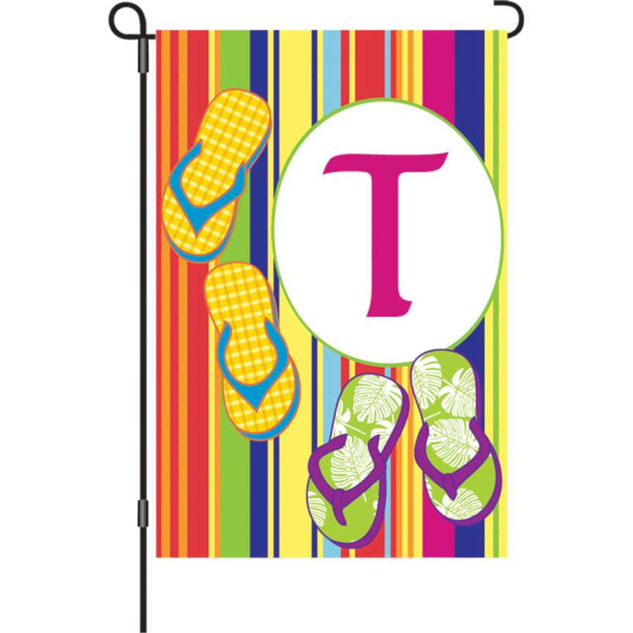 12 in. Summer Monogram Flag featuring the letter 'T' with a colorful summer design, displayed on a garden flag stand surrounded by flowers and greenery.
