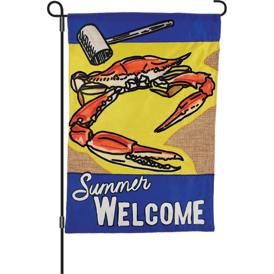 12 in. Summer Welcome flag featuring colorful crab and mallet design, celebrating Old Bay seasoning, displayed outdoors in a garden setting.