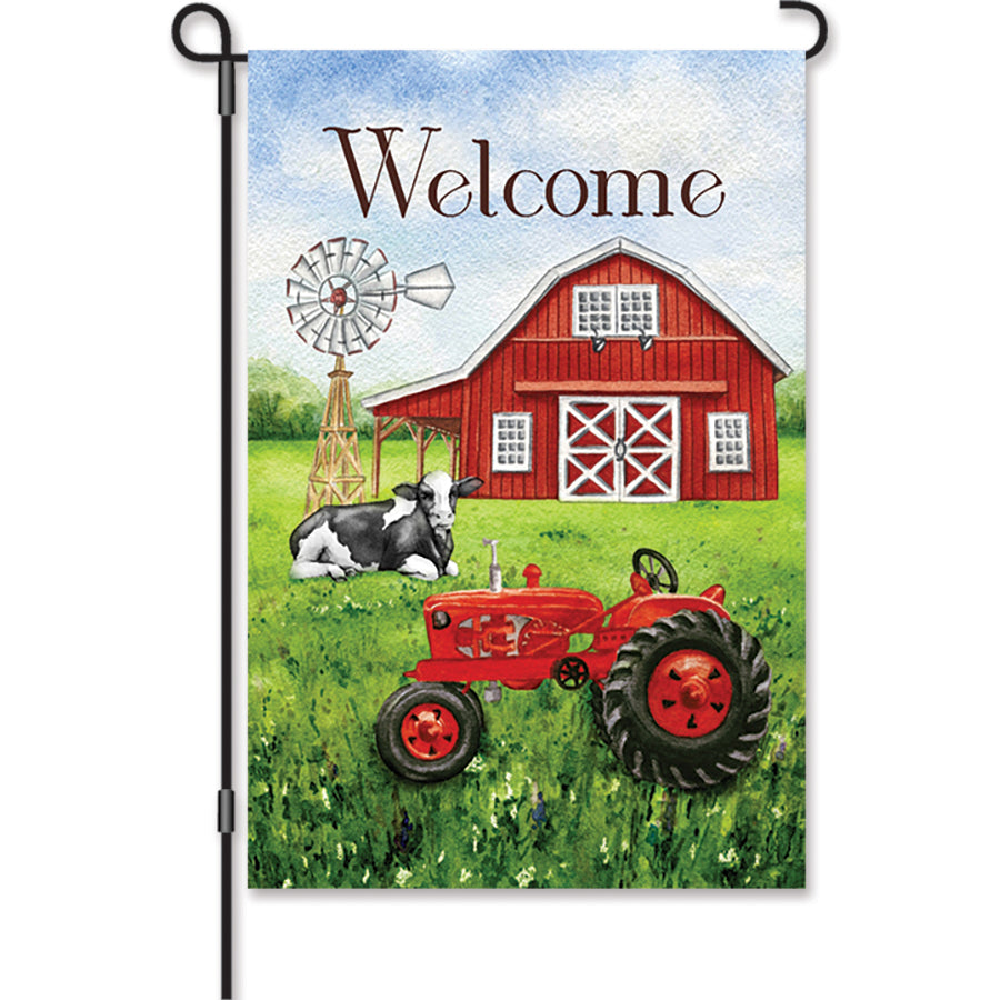 12 in. Welcome Farm flag displaying a charming welcome message on a soft fabric, fluttering gently in an outdoor garden setting.