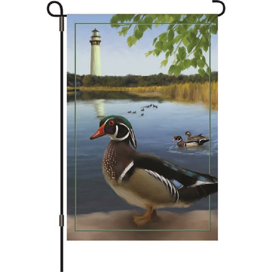 12 in. illuminated garden flag featuring vibrant wood ducks design, displayed outdoors on a garden flag stand during evening hours, glowing softly.