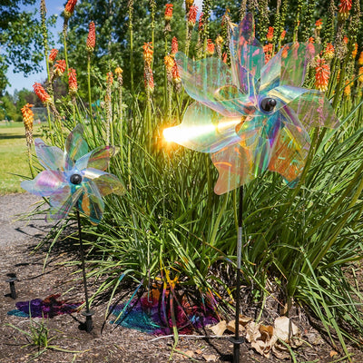 12-inch iridescent pinwheel spinner displayed in a garden, featuring colorful Mylar petals that catch the wind and reflect sunlight.
