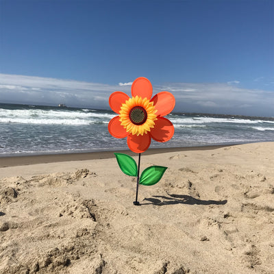 12-inch orange sunflower spinner with bright petals and green leaves, spinning on a sturdy fiberglass pole in a garden setting.