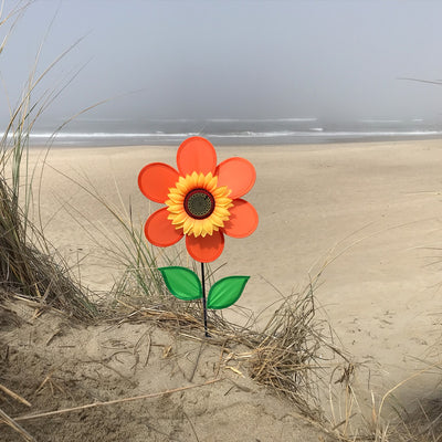 12-inch orange sunflower spinner with bright petals and green leaves, spinning on a sturdy fiberglass pole in a garden setting.